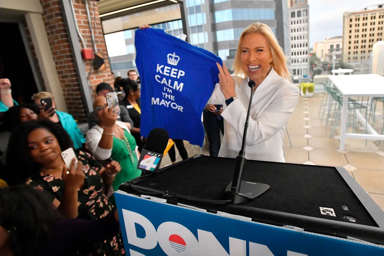 Donna Deegan smiles at a podium while holding a shirt that reads Keep Calm I'm the Mayor